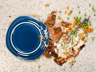 A plate of meatloaf with mashed potatoes and peas dropped on new carpet.