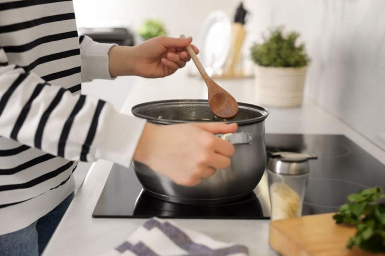 Woman with wooden spoon cooking soup in kitchen, closeup